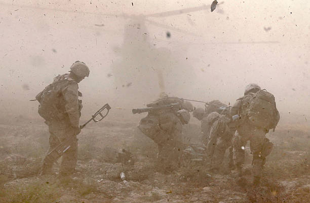 US soldiers in Afghanistan crouch as a helicopter lands and debris flies around.